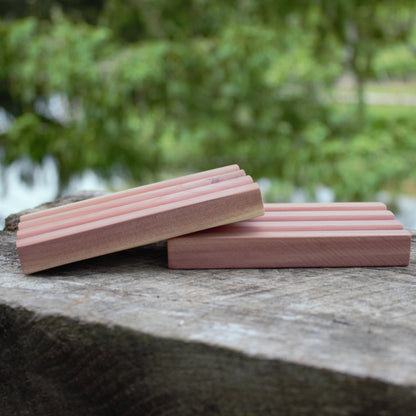 side view of two cedar soap trays on wood with natural green background