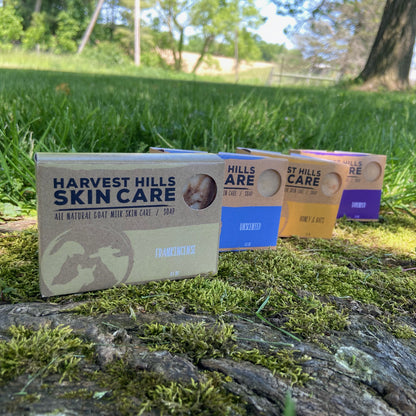 Harvest Hills Skin Care goat milk soaps on a wooden log with grass and trees in the background