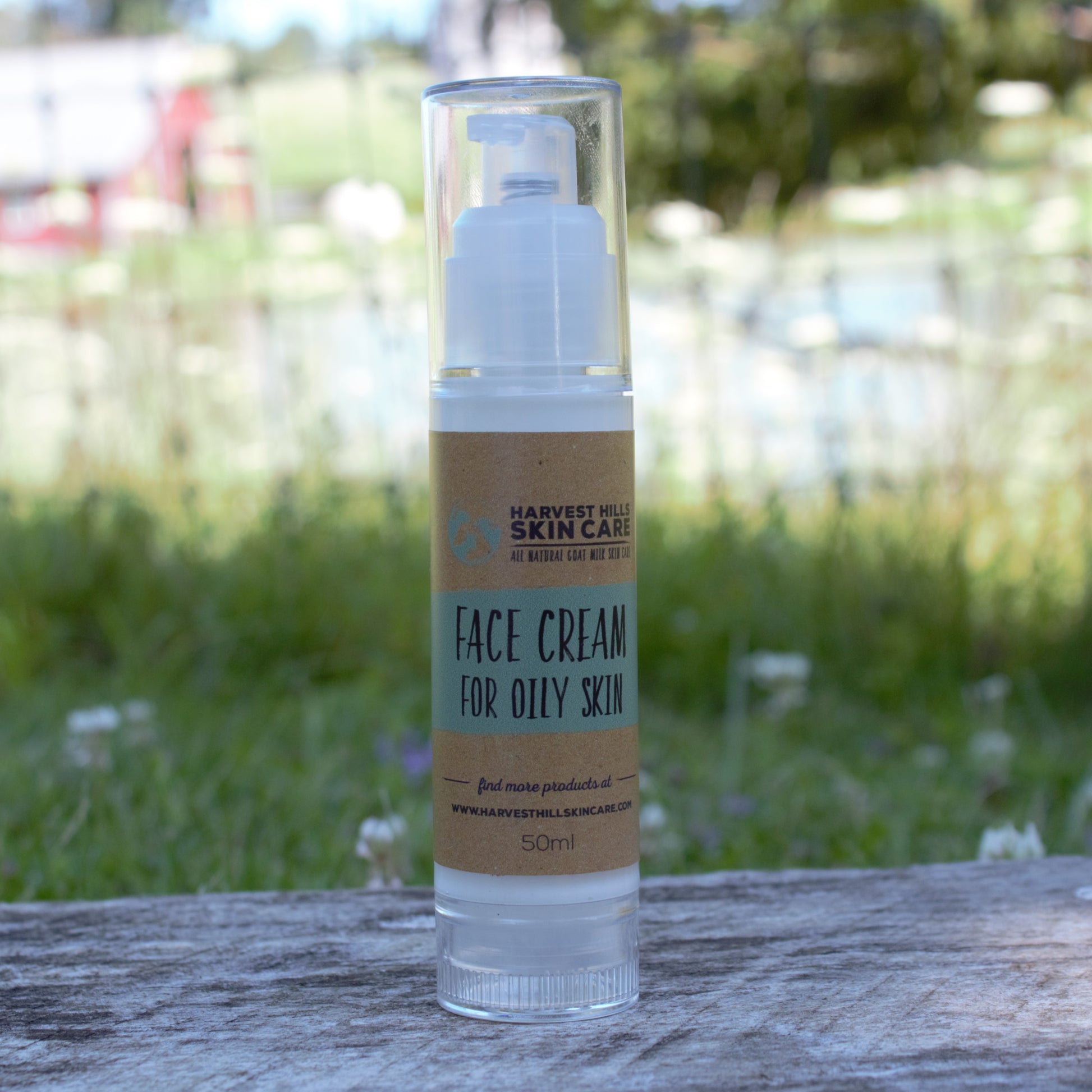 A 50ml bottle of Harvest Hill Skin Care Face Cream for Oily Skin, featuring a clear cylindrical container and a brown paper label, set on a weathered wooden surface with a blurred green garden background.
