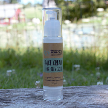 A 50ml bottle of Harvest Hill Skin Care Face Cream for Oily Skin, featuring a clear cylindrical container and a brown paper label, set on a weathered wooden surface with a blurred green garden background.