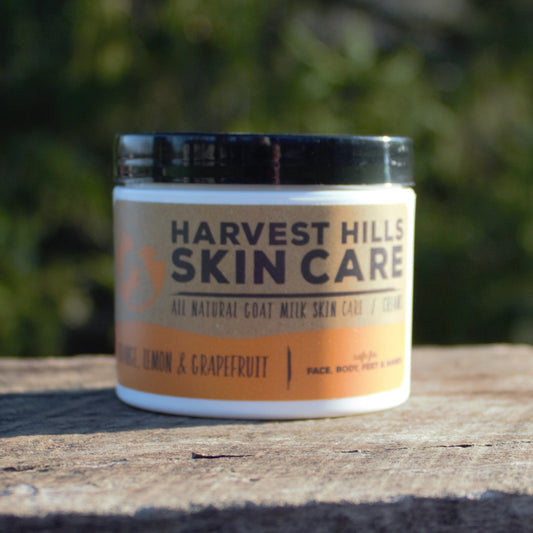 Jar of Harvest Hills Skin Care goat milk moisturizer on a wooden surface with a blurred green background